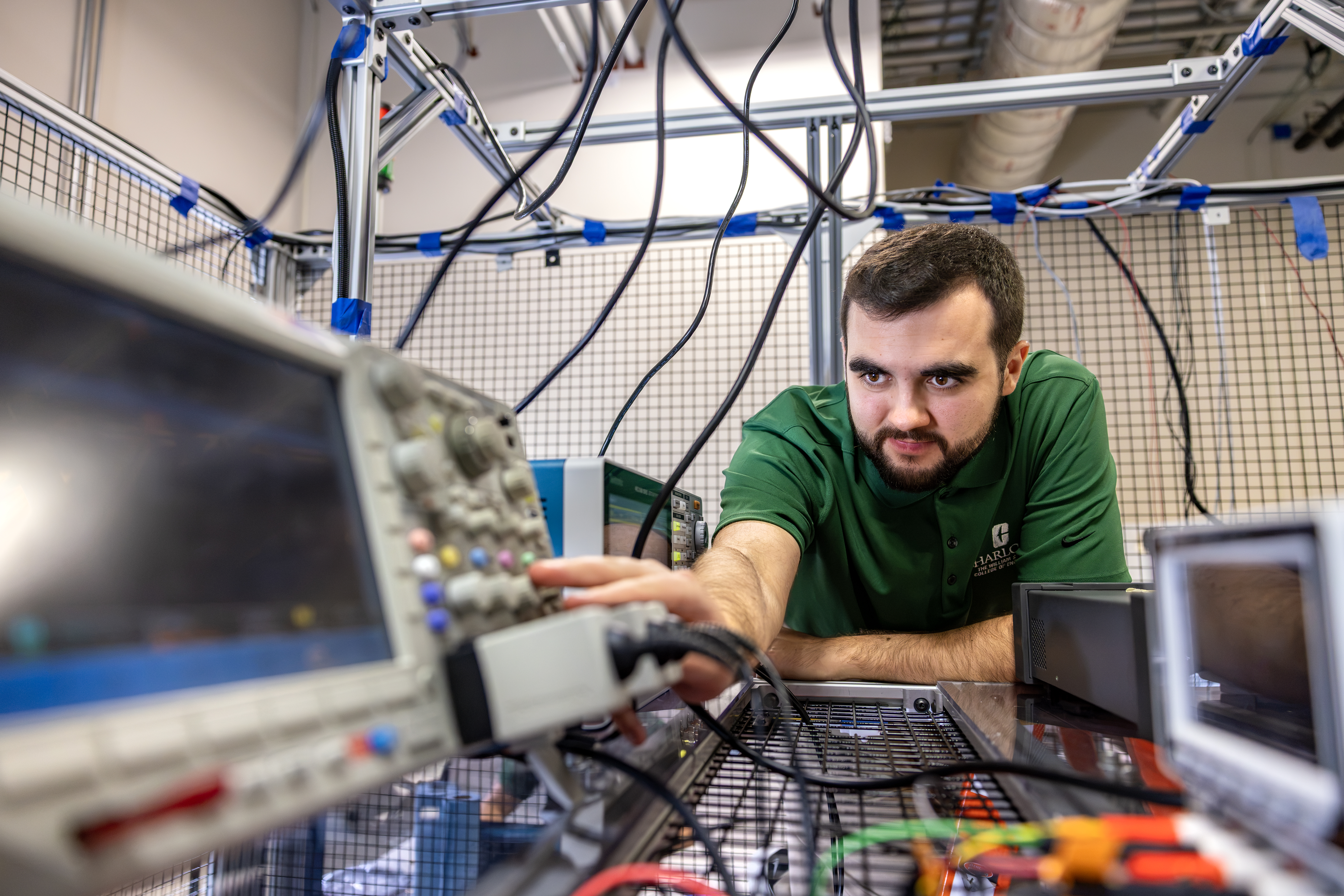 UNC Charlotte student wearing a College of Engineering polo leans over and adjusts equipment in EPIC Lab