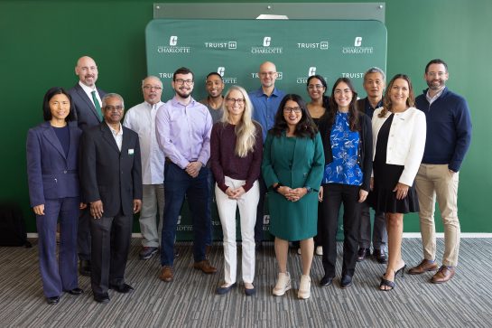 2026 Truist Report - Research Symposium A group of faculty, staff, and partners pose together in front of a University of North Carolina at Charlotte and Truist-branded backdrop during a campus event. The group stands smiling for a photo in a bright meeting space.