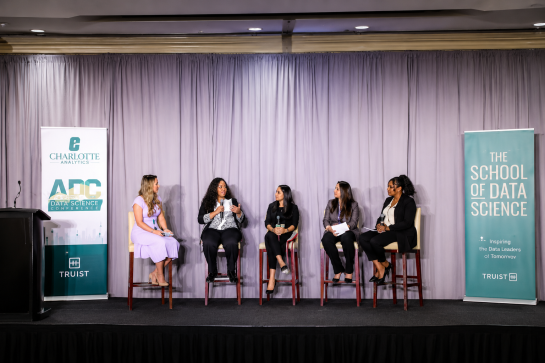 2026 Truist Report - WIDS 1 Five panelists sit on stage during the Charlotte Analytics ADC Data Science Conference, participating in a discussion between banners for Charlotte Analytics and The School of Data Science.