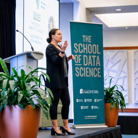 2026 Truist Report - WIDS 2 A speaker presents on stage at a data science conference beside a podium and a banner reading “The School of Data Science.”