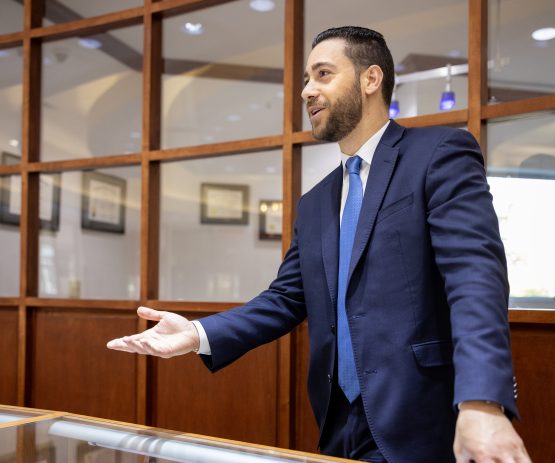 Man in a navy blue suit standing behind a jewelry display case.