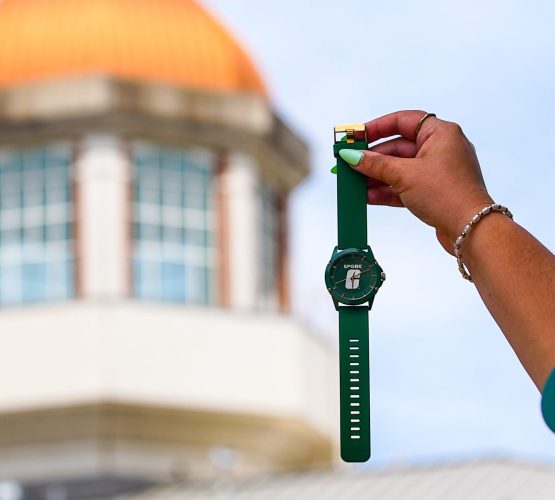 SPGBK-Watch-1 Hand holding a green UNC Charlotte watch in front of the blurred dome.