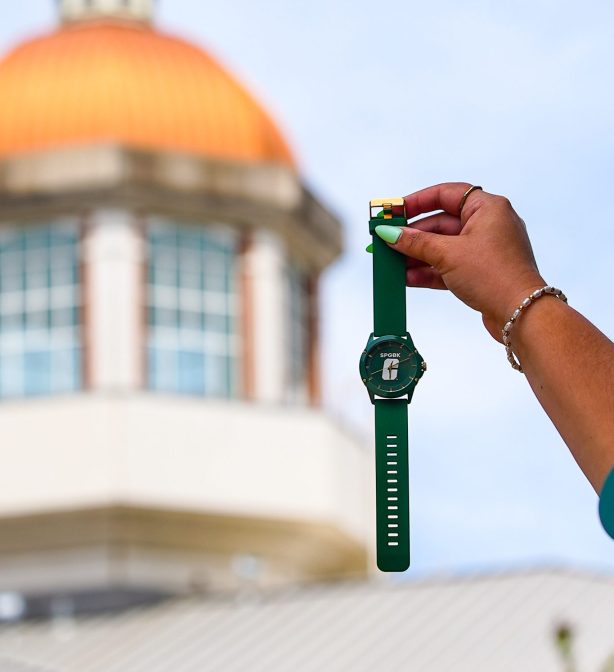 SPGBK-Watch-1 Hand holding a green UNC Charlotte watch in front of the blurred dome.