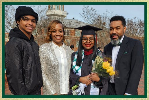 Graduate in cap and gown holds a bouquet of flowers while posing with three family members on a brick campus walkway, with a domed building in the background.