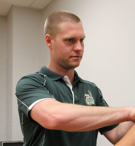 Hendricks_OrthoCarolina2 An athletic trainer wearing a green 49ers polo evaluates a student's shoulder and arm during a clinical assessment in a sports medicine laboratory.
