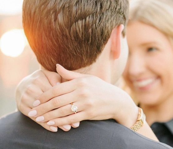 Woman hugging a man, showing hands with a diamond ring on his shoulder.