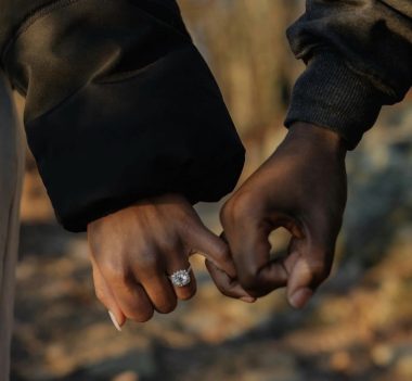 Two people linking their pinky fingers, one wearing a sparkling ring.