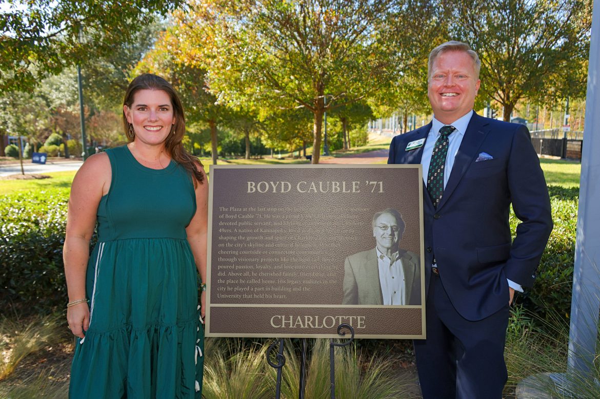 Bo and Angie Cauble stand in front of the plaque honoring Bo's dad, Boyd, near the light rail platform. {{brizy_dc_image_alt imageSrc=