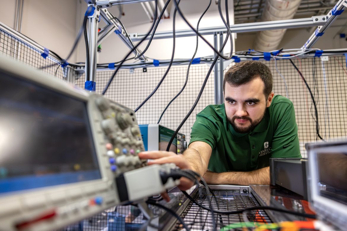UNC Charlotte student wearing a College of Engineering polo leans over and adjusts equipment in EPIC Lab