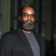 Portrait of a UNC Charlotte student wearing glasses and a blazer, standing in a dimly lit indoor space. {{brizy_dc_image_alt imageSrc=
