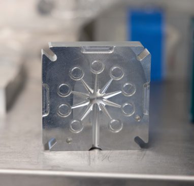 Close-up of a machined metal block with circular channels and precision-cut features on a work surface.