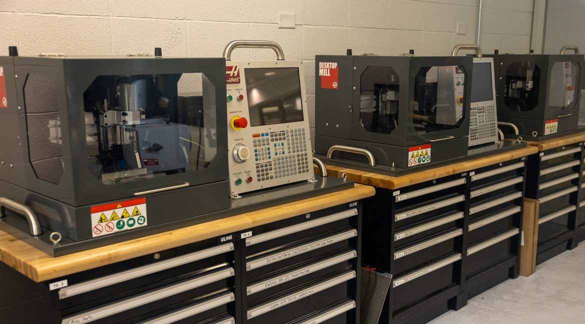 Haas desktop milling machines arranged on a workbench in a machine shop environment.