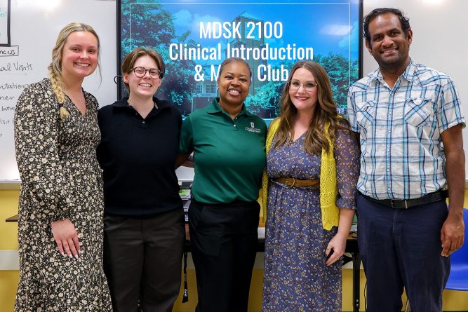Five educators and students standing together in a classroom in front of a screen displaying “Clinical Introduction & Media Club,” smiling for a group photo.