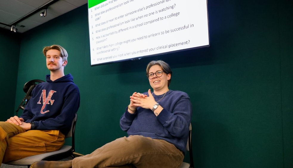 Two speakers seated in front of a screen presenting questions and leading a discussion with an audience.