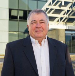 A well-dressed man in a suit and tie poses in front of a sleek building, showcasing a professional demeanor.