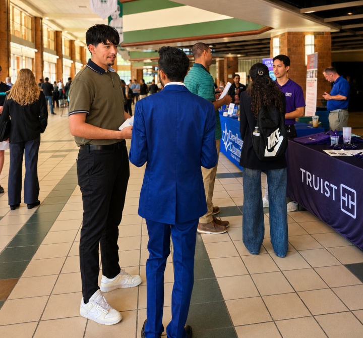 Truist Image 1 Students and recruiters network at a university career fair inside a large campus atrium, with a Truist information table and a digital display promoting a computing and informatics alumni panel.